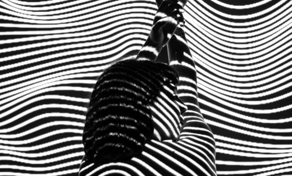 Person silhouetted against wavy black-and-white projection lines