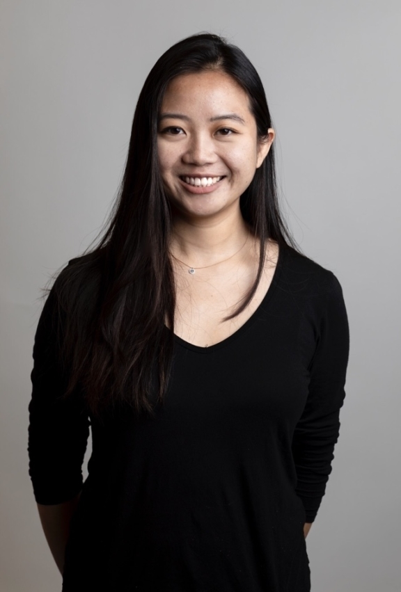 Smiling woman in a black top standing against a gray studio background.